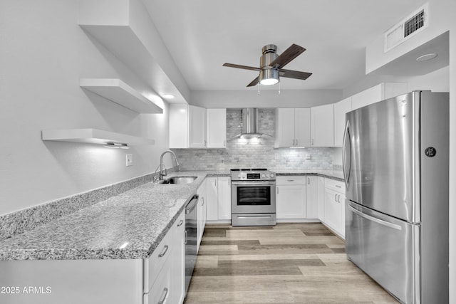 kitchen with visible vents, appliances with stainless steel finishes, a sink, light stone countertops, and wall chimney exhaust hood