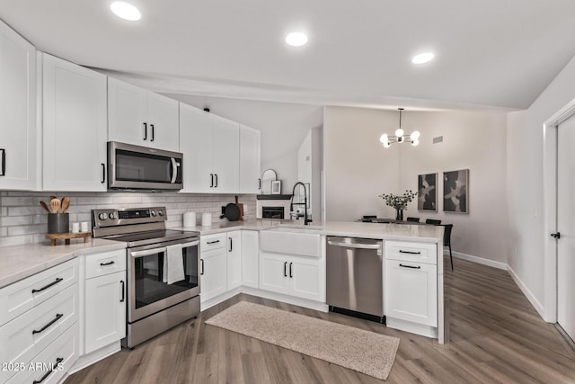 kitchen featuring white cabinets, appliances with stainless steel finishes, sink, kitchen peninsula, and vaulted ceiling