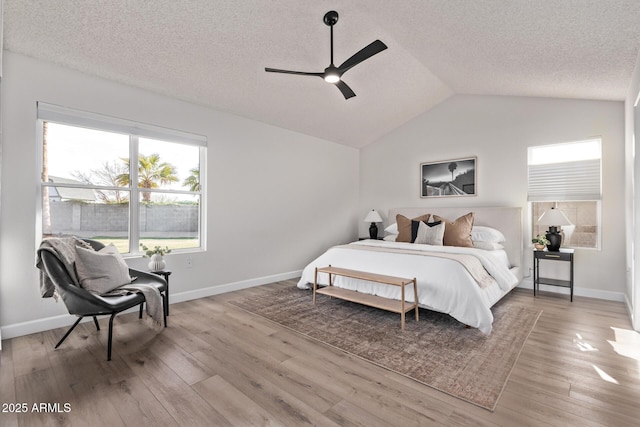 bedroom featuring ceiling fan, a textured ceiling, light hardwood / wood-style flooring, and lofted ceiling