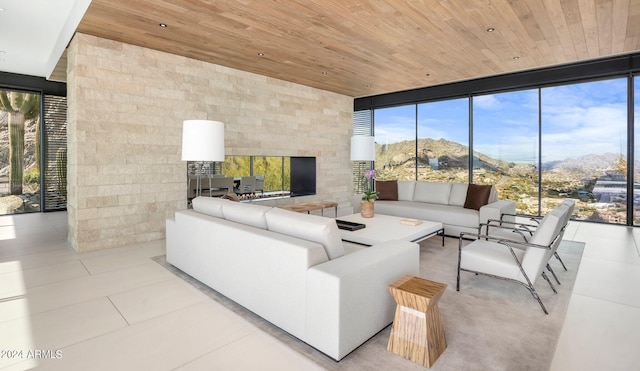 living room with wood ceiling, a mountain view, a fireplace, light tile patterned floors, and a wall of windows