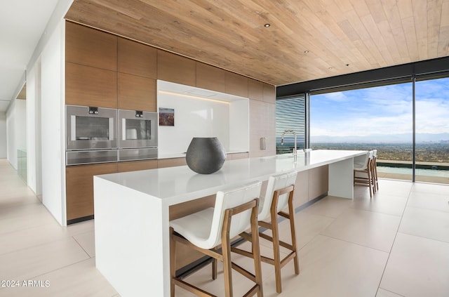 kitchen featuring expansive windows, a breakfast bar area, a kitchen island with sink, and wooden ceiling