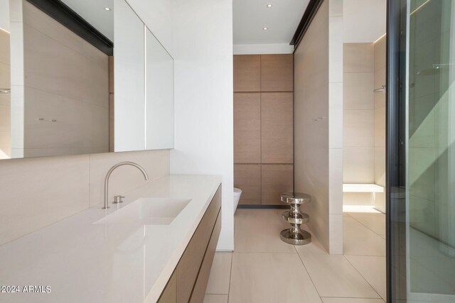 bathroom with tile walls, a shower with door, tile patterned floors, vanity, and toilet