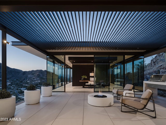 patio terrace at dusk with a mountain view, an outdoor kitchen, and an outdoor living space with a fire pit