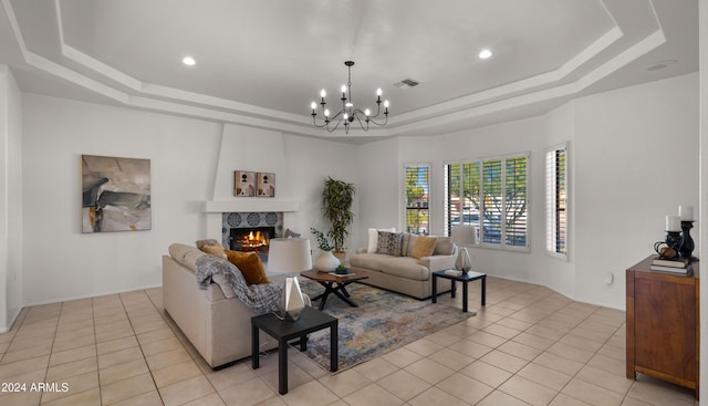 tiled living room with a raised ceiling, a large fireplace, and an inviting chandelier