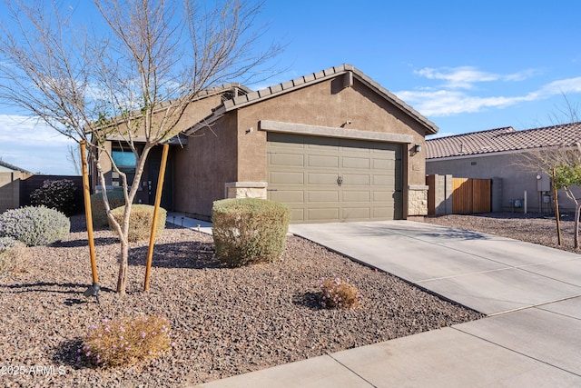 view of side of home with a garage, fence, driveway, a tiled roof, and stucco siding