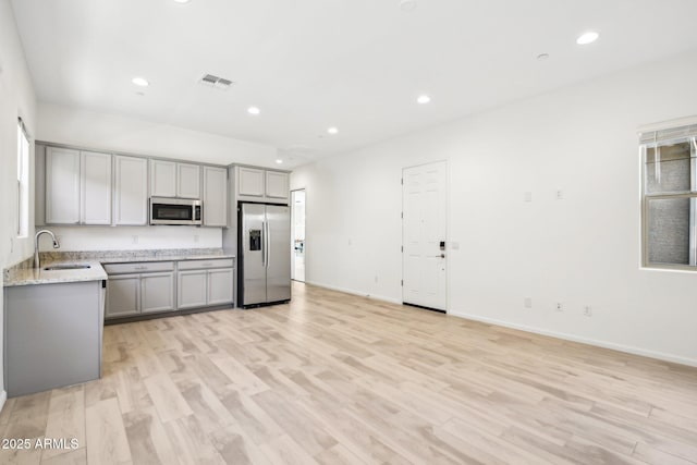 kitchen with gray cabinetry, sink, light stone countertops, and appliances with stainless steel finishes