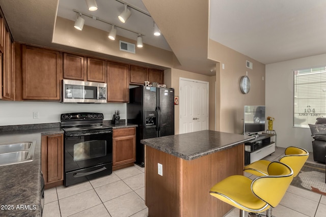 kitchen with black appliances, light tile patterned floors, a kitchen bar, and a center island