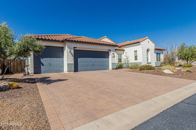 mediterranean / spanish-style home featuring a tile roof, decorative driveway, a garage, and stucco siding