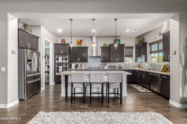 kitchen featuring dark brown cabinetry, wall chimney exhaust hood, appliances with stainless steel finishes, and a center island