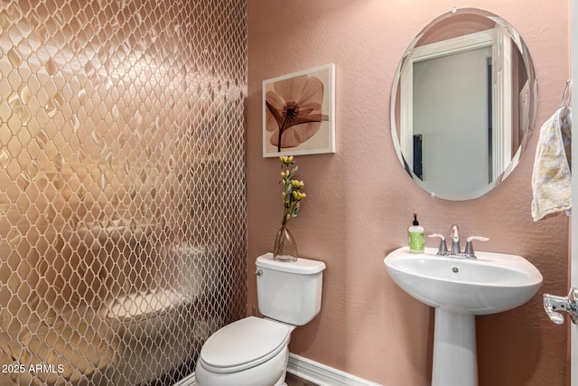 bathroom featuring baseboards, toilet, and a textured wall