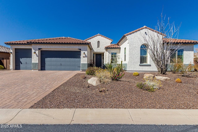 mediterranean / spanish house with stucco siding, decorative driveway, an attached garage, and a tile roof