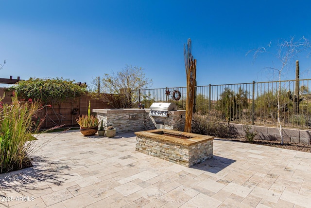 view of patio featuring a fenced backyard, a fire pit, area for grilling, and exterior kitchen