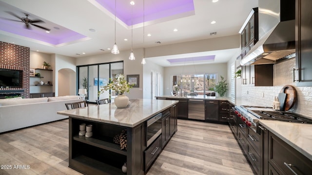 kitchen featuring light stone counters, wall chimney exhaust hood, a tray ceiling, and decorative light fixtures