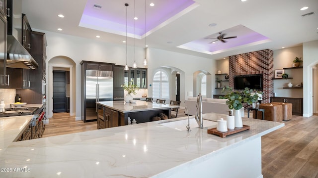 kitchen with decorative light fixtures, a kitchen island with sink, stainless steel built in fridge, and a tray ceiling