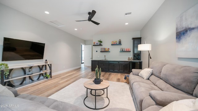 living room with ceiling fan, bar area, and light hardwood / wood-style flooring