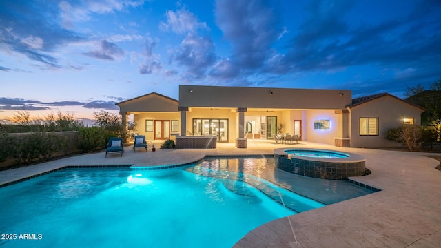 pool at dusk featuring a patio, ceiling fan, and an in ground hot tub