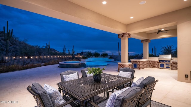 patio terrace at dusk with area for grilling, a grill, ceiling fan, and an in ground hot tub