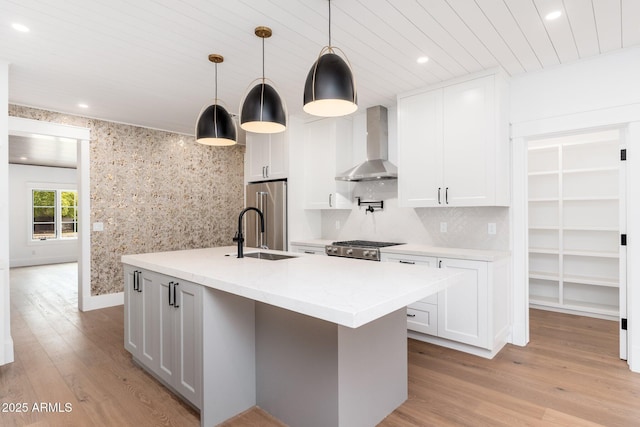 kitchen with pendant lighting, white cabinetry, sink, and wall chimney range hood