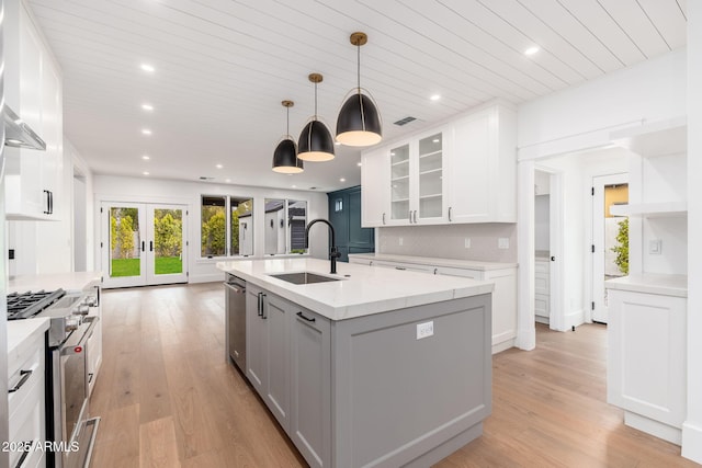 kitchen with appliances with stainless steel finishes, an island with sink, sink, white cabinets, and french doors