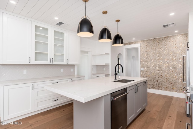 kitchen with sink, hardwood / wood-style flooring, white cabinetry, hanging light fixtures, and a kitchen island with sink