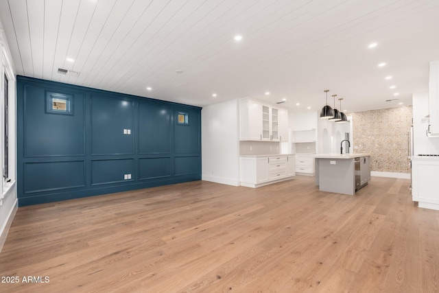 interior space featuring white cabinetry, hanging light fixtures, wood ceiling, a center island with sink, and light wood-type flooring