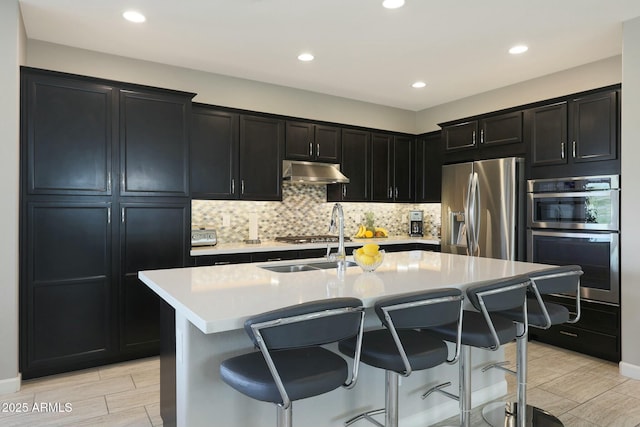 20702 W Hillcrest Blvd, Buckeye, AZ 85396 - kitchen featuring appliances with stainless steel finishes, under cabinet range hood, dark cabinets, a kitchen breakfast bar, and recessed lighting
