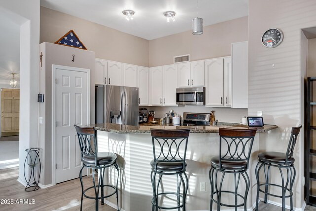 kitchen with dark stone countertops, appliances with stainless steel finishes, a kitchen breakfast bar, kitchen peninsula, and white cabinets