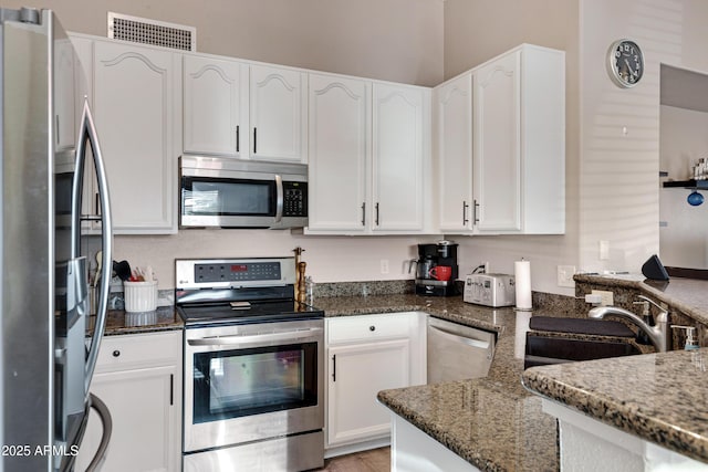 kitchen featuring white cabinetry, stainless steel appliances, and dark stone counters