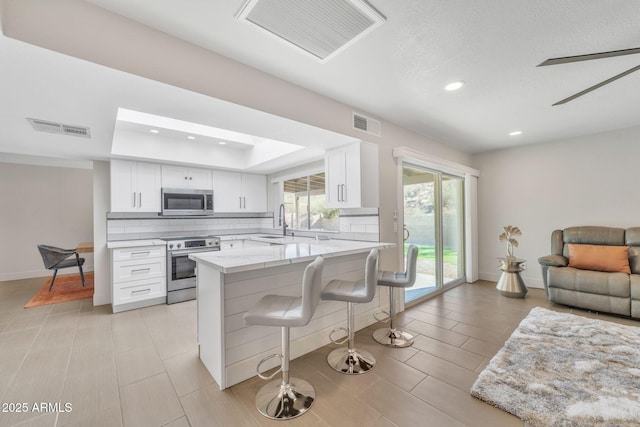 kitchen with white cabinetry, sink, stainless steel appliances, a kitchen breakfast bar, and light stone counters