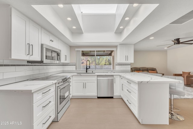 kitchen with a kitchen bar, appliances with stainless steel finishes, kitchen peninsula, sink, and white cabinetry