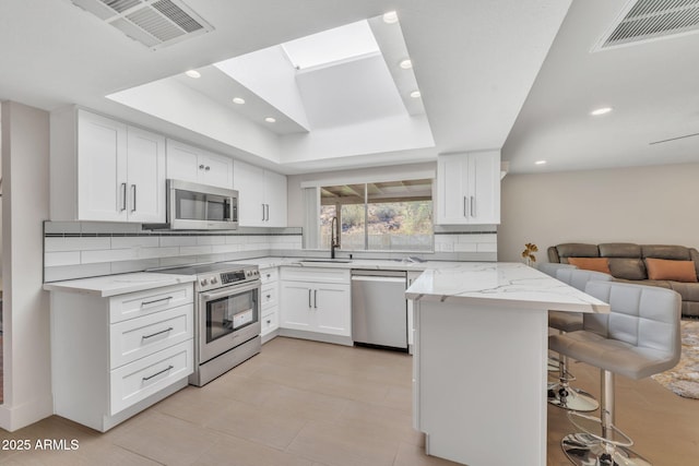 kitchen featuring kitchen peninsula, a tray ceiling, a kitchen bar, white cabinets, and appliances with stainless steel finishes