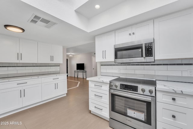 kitchen with white cabinets, decorative backsplash, light stone counters, and stainless steel appliances