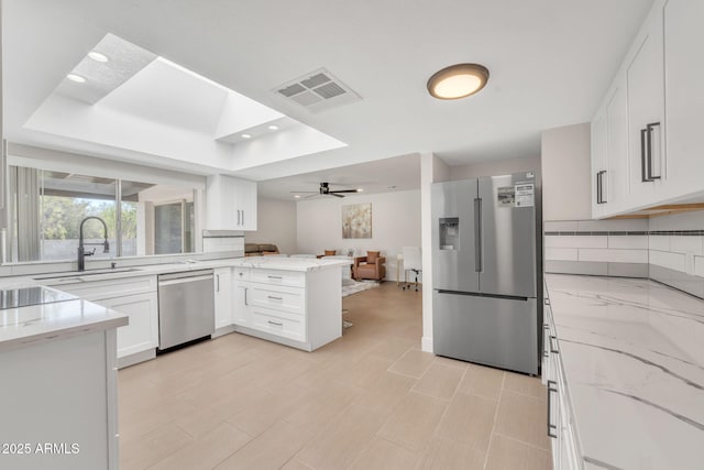 kitchen with ceiling fan, stainless steel appliances, light stone counters, kitchen peninsula, and white cabinets