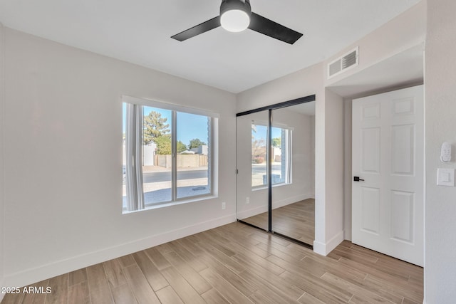 unfurnished bedroom with ceiling fan, light hardwood / wood-style floors, multiple windows, and a closet