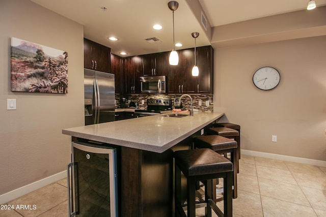 kitchen featuring a sink, a peninsula, wine cooler, a breakfast bar area, and appliances with stainless steel finishes
