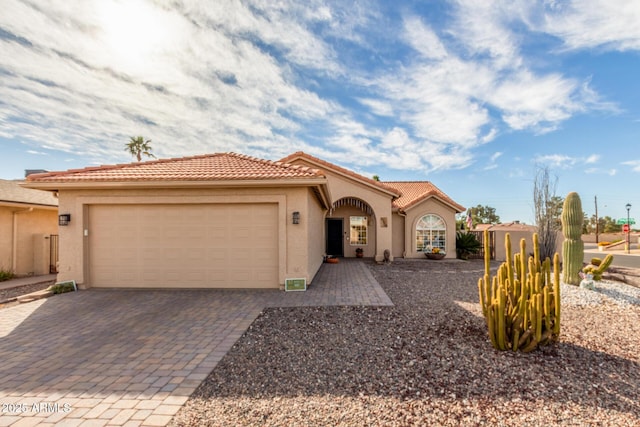 mediterranean / spanish house featuring a garage, a tiled roof, decorative driveway, and stucco siding