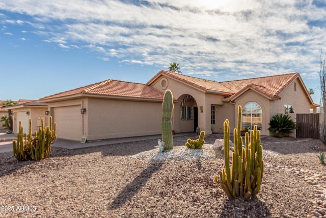 mediterranean / spanish home featuring a garage, stucco siding, a tile roof, and fence