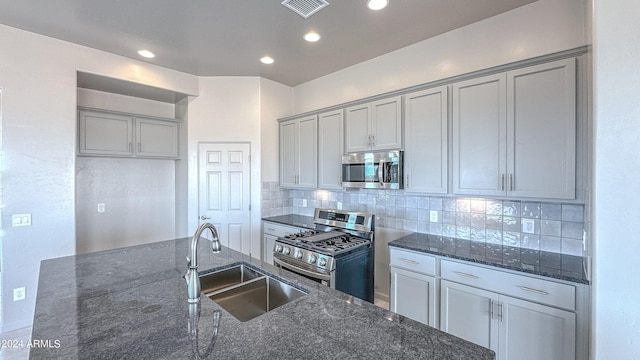 kitchen with sink, stainless steel appliances, dark stone countertops, and gray cabinetry