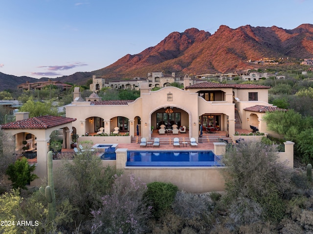 back house at dusk featuring a mountain view and a patio