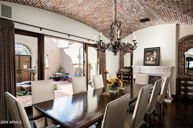 dining space featuring a chandelier, dark hardwood / wood-style flooring, lofted ceiling, and brick ceiling