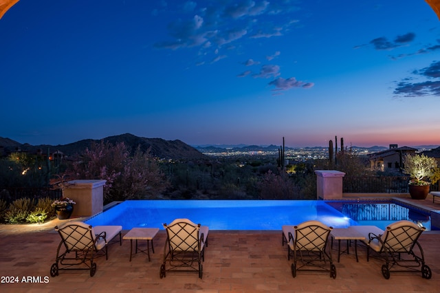 pool at dusk featuring a mountain view and a patio