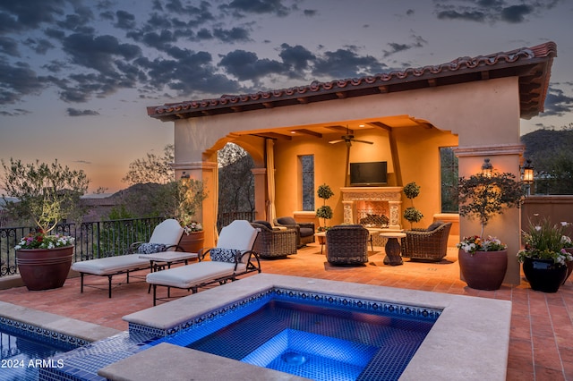 pool at dusk with ceiling fan, a patio, and exterior fireplace