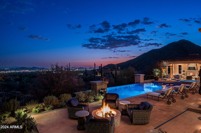 pool at dusk with a mountain view, a patio, and an outdoor fire pit