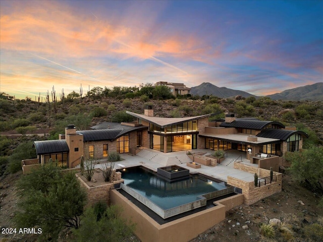 back house at dusk featuring a mountain view, a patio, and a pool with hot tub