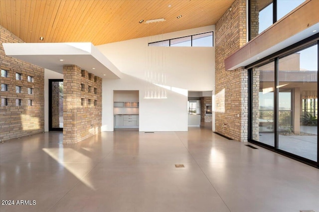 unfurnished living room with high vaulted ceiling, brick wall, wood ceiling, and concrete floors