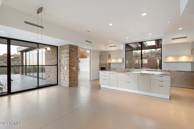 kitchen featuring stainless steel oven, white cabinetry, pendant lighting, floor to ceiling windows, and a skylight