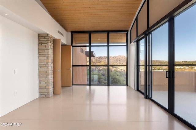 unfurnished room with wooden ceiling, a wall of windows, a mountain view, and decorative columns