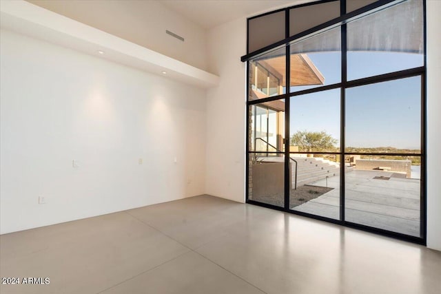 empty room featuring a towering ceiling, a wall of windows, and concrete floors