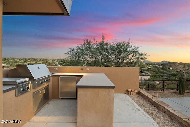 patio terrace at dusk featuring area for grilling, a mountain view, and exterior kitchen