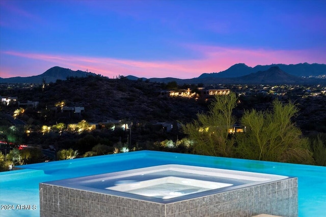 pool at dusk with a mountain view and an in ground hot tub